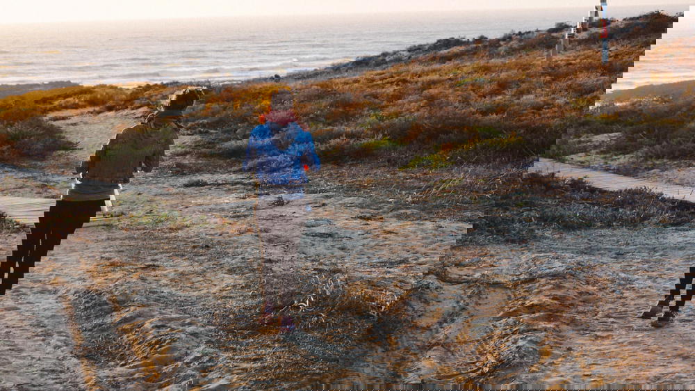 A woman is walking down a path near the ocean.