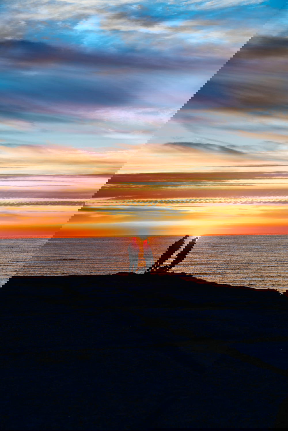 Two people at the edge of a rock during sunset at a beach