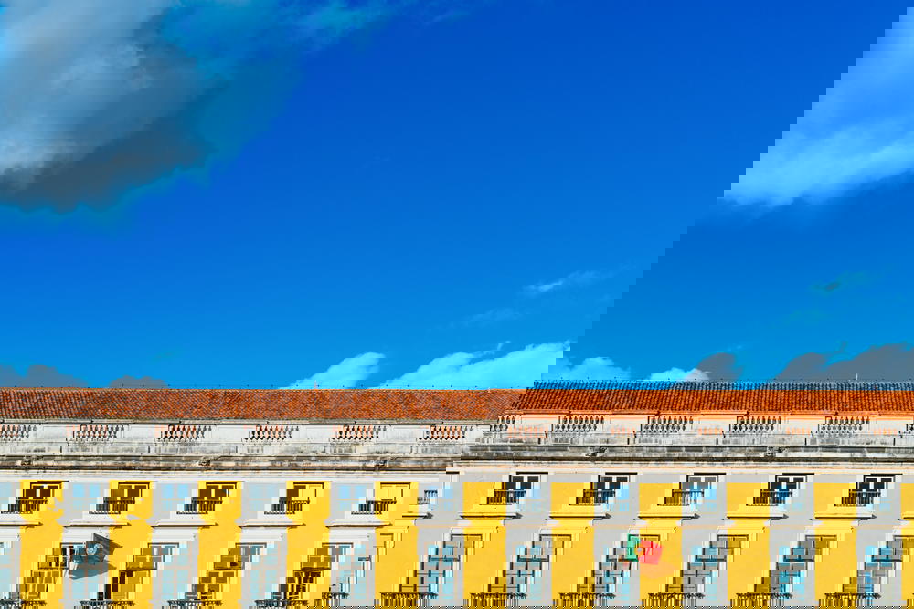 Yellow facade of a historic Portuguese building and red tiled rooftop against bright blue sky