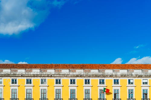 Yellow facade of a historic Portuguese building and red tiled rooftop against bright blue sky