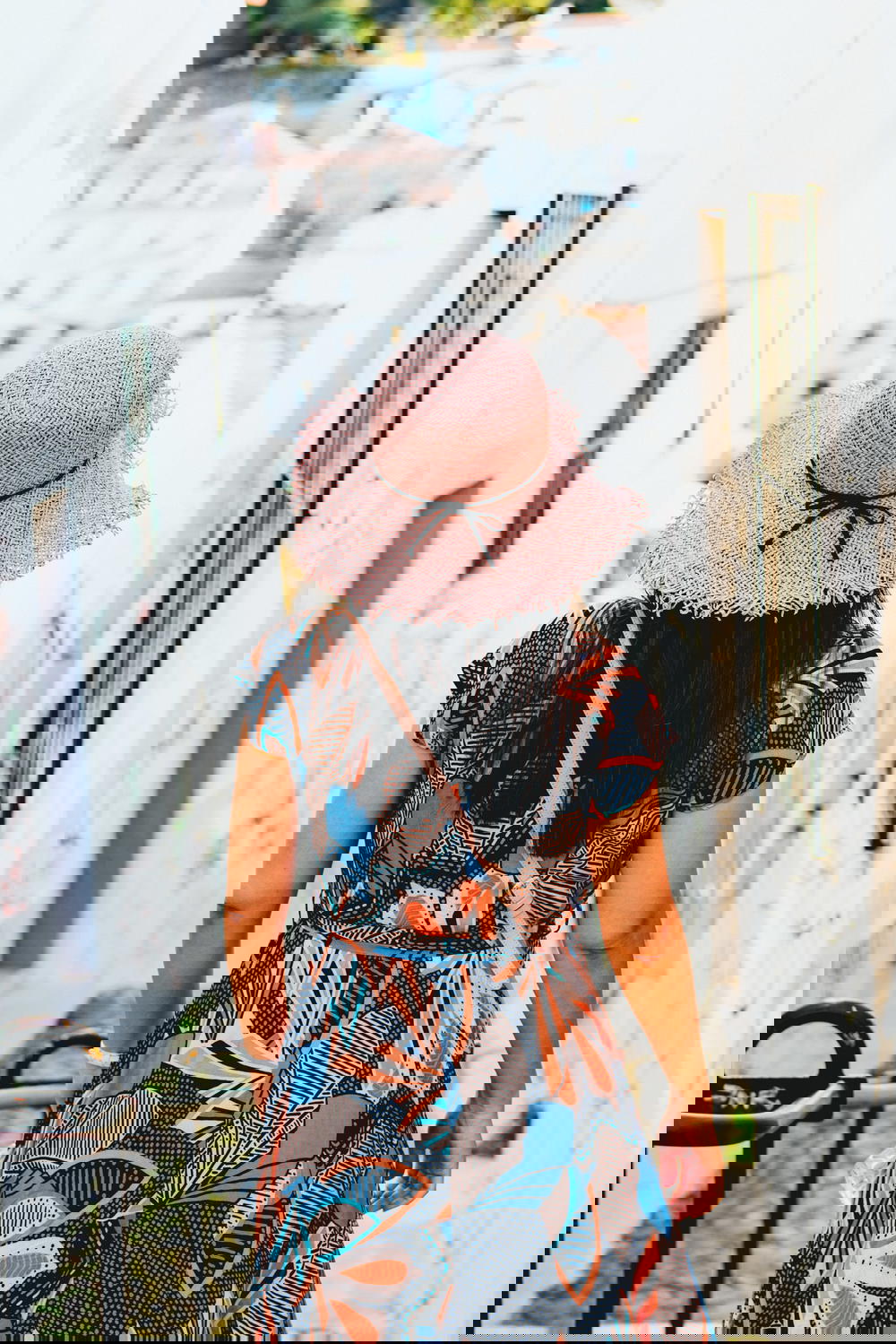 A woman wearing a pink hat and floral dress walking down a cobbled street.