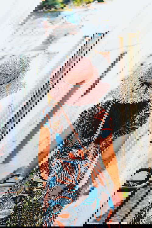 A woman wearing a pink hat and floral dress walking down a cobbled street.