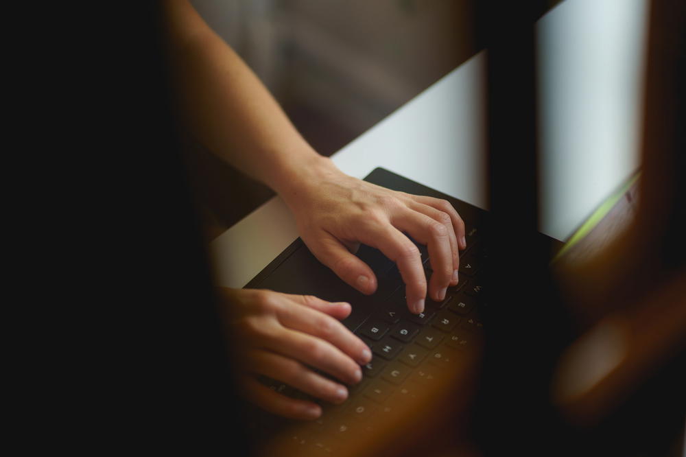 Woman typing on a black 13 inch laptop keyboard in a small apartment home office