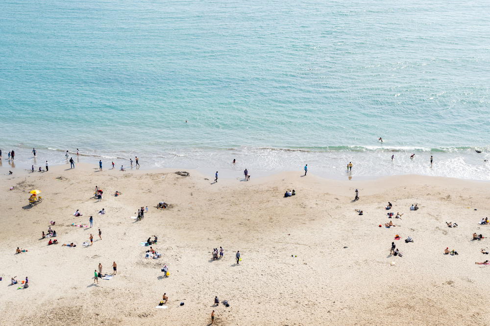 People on a beach next to light blue ocean water