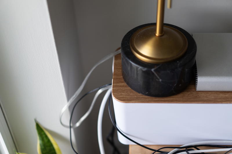 The base of a small desk lamp on top of a cable management box.