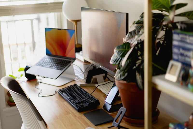 A work from home desk with a laptop, monitor, keyboard and a plant.