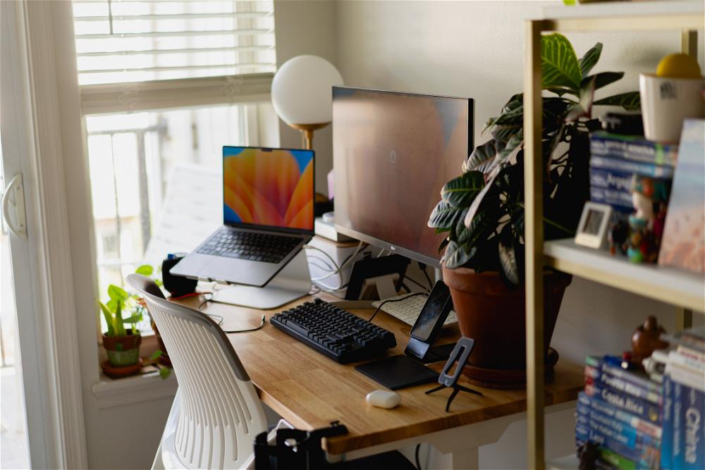A work from home desk with a laptop, monitor, keyboard and a plant.