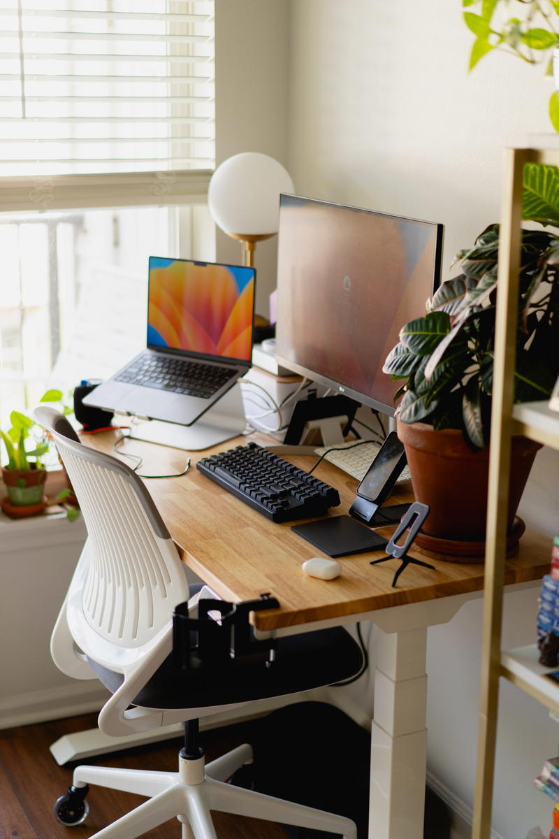 A work from home desk with a laptop, monitor, keyboard and a plant.