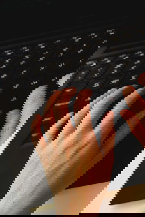 Two hands typing on a black laptop keyboard at a white desk