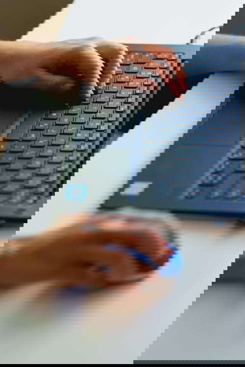 Typing and working from home with a laptop at a small white desk in a home office