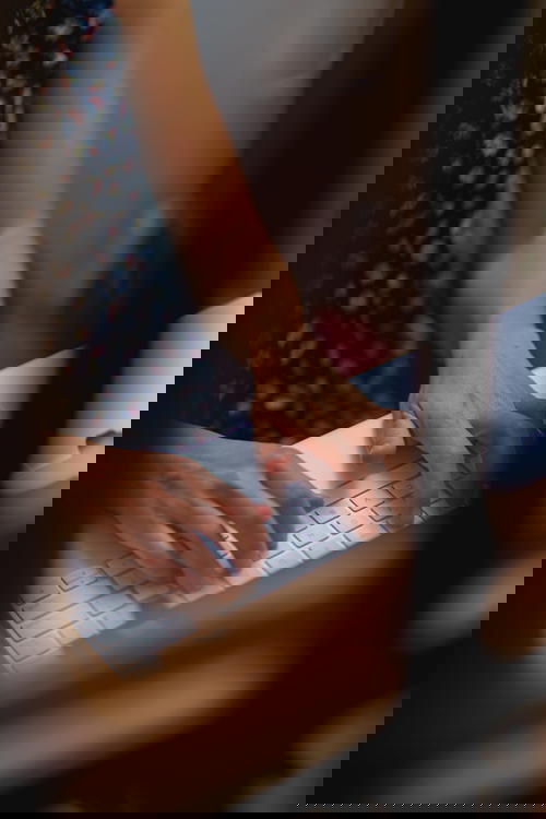 Woman typing on an Apple Magic keyboard at a white desk table in a home office