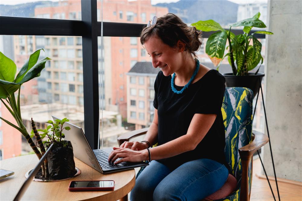 Woman working remotely from a laptop at a round wooden table in a coworking space with plants