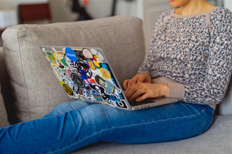 Woman working on a couch with a laptop with stickers