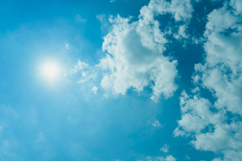 Sunlight and puffy white clouds against a clear blue sky