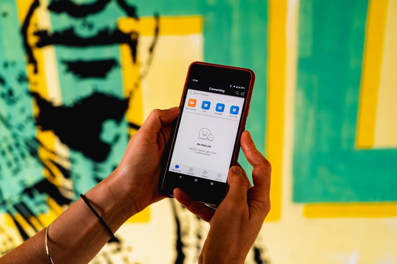 Two hands holding the Zoom app interface on a google pixel phone in front of a green and yellow wall