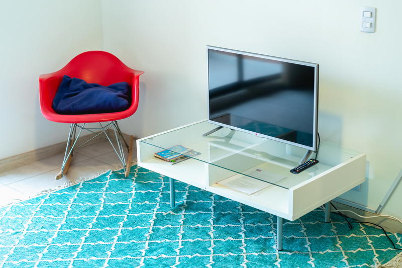 Red bucket chair with a blue pillow next to a white and glass entertainment unit and a flat screen tv