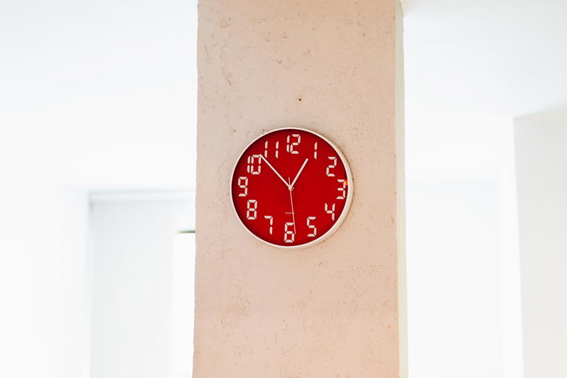 Red analog clock with digital style numbers on a beige wall in a white room
