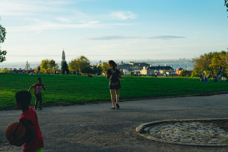 Woman walking on a sidewalk in a grassy park at golden hour in a city
