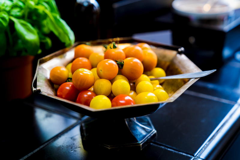 Round orange cherry tomatoes in a brass pedestal bowl on a tiled countertop