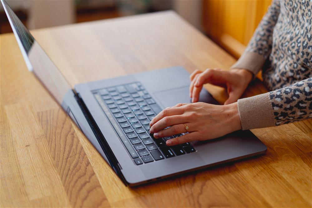 Woman's hand using a 16 inch MacBook Pro on a wooden counter