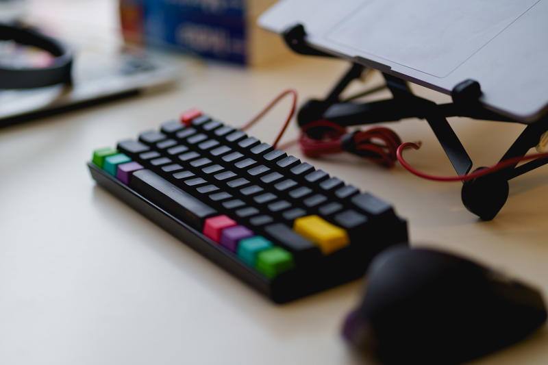 Black keyboard with a wireless bluetooth mouse on a standing desk with a laptop on a laptop stand