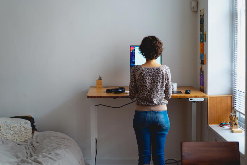 Woman standing and working from home at a bamboo standing desk next to a window in a home workspace