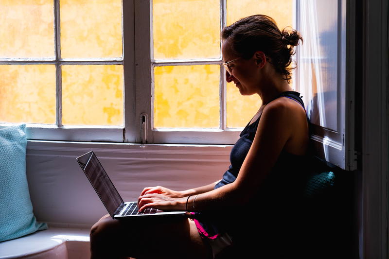 Woman sitting in a window seat working remotely from a black laptop in Tenerife
