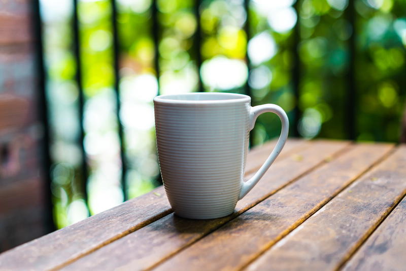 White coffee cup set on a wooden outdoor deck table with green trees in the background
