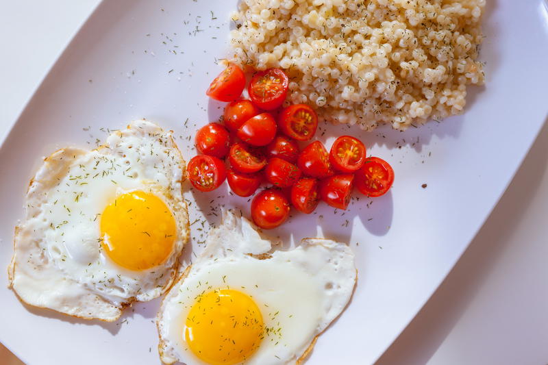 White rectangular plate with two fried eggs, sauteed grape tomatoes and couscous sprinkled with herbs