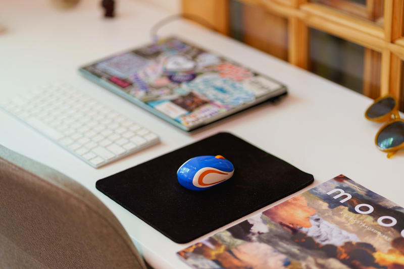 Mini Logitech computer mouse on a black mousepad next to a laptop on a small white desk from a home office
