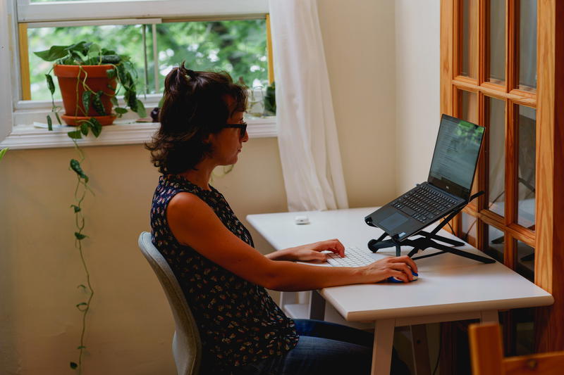 Woman using a laptop stand with a laptop on a small compact white desk in a home office in an apartment