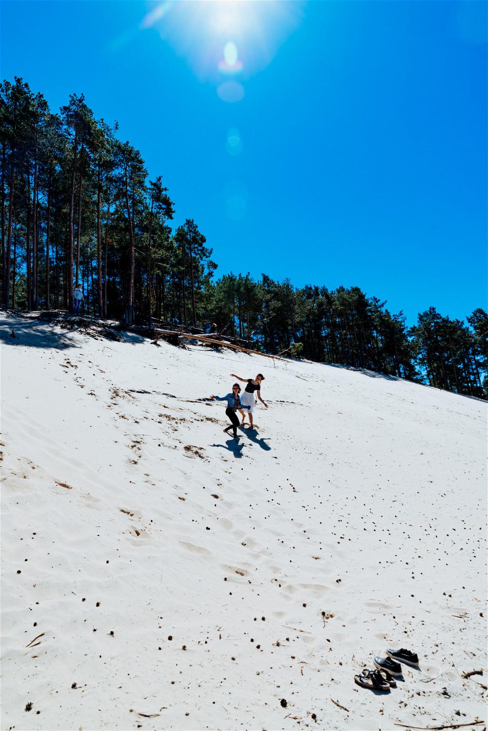 Two girls surfing down a big white sand dune