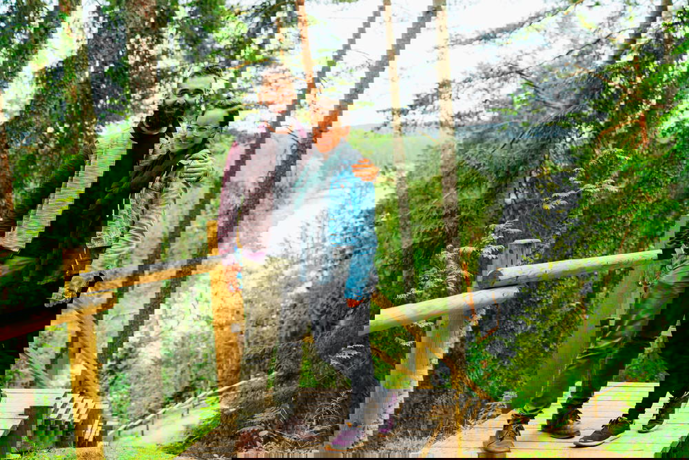 A man and woman standing on a wooden walkway in a forest.