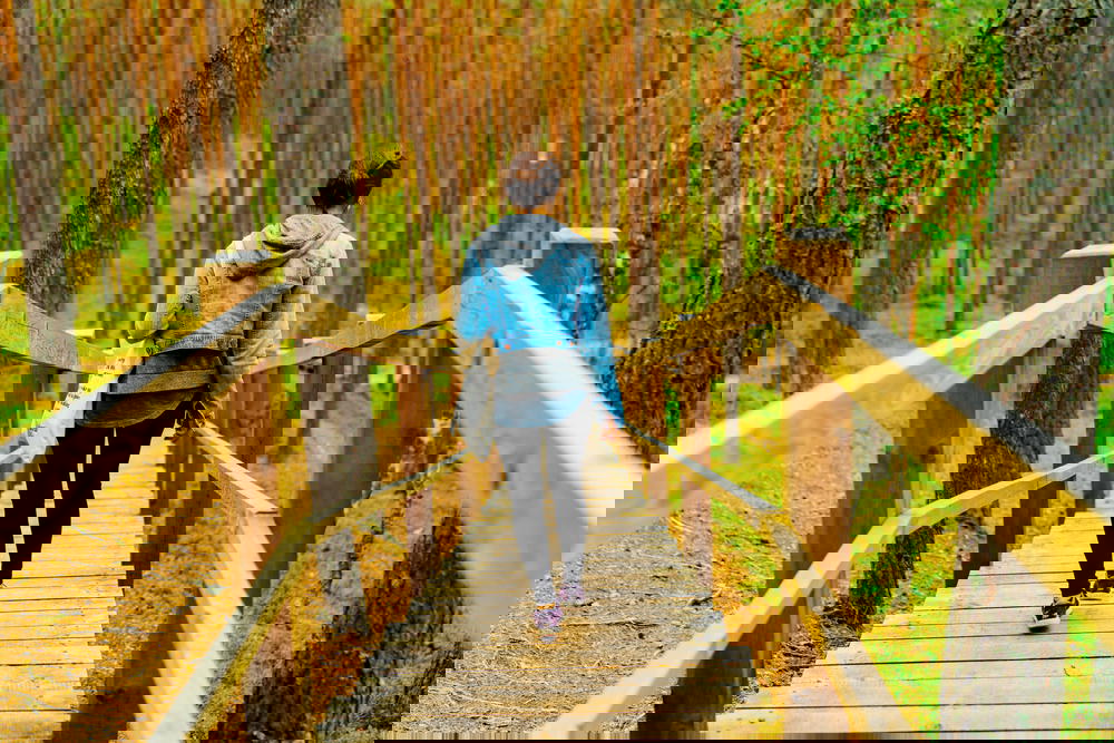 A woman is walking down a wooden walkway in a forest.