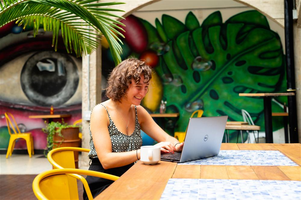 A woman sitting at a table with a laptop in front of a mural.