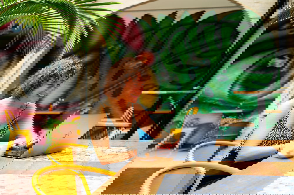 A woman sitting at a table with a laptop in front of a mural.
