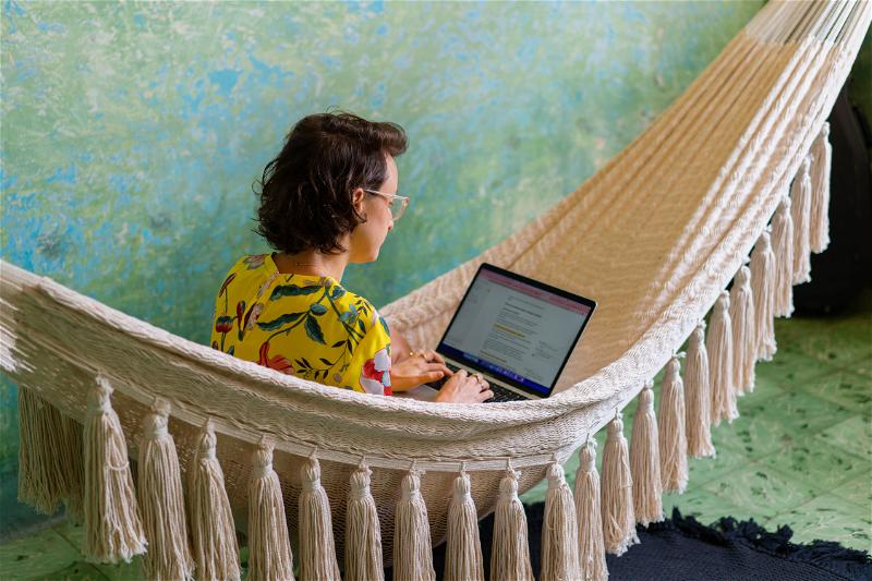 A woman using a laptop in a hammock.
