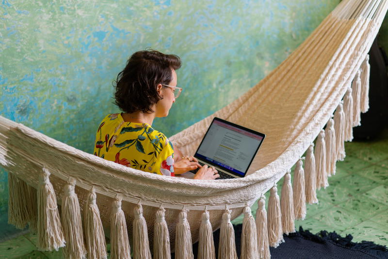 A woman using a laptop in a hammock.