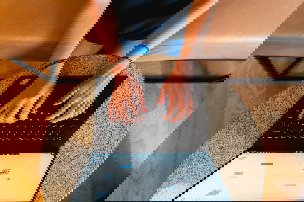 Woman sitting on a beige bench working remotely at a laptop at a small circular granite table