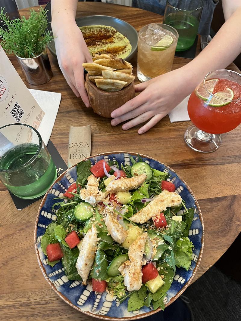 A plate of chicken salad with chips and drinks on a table.