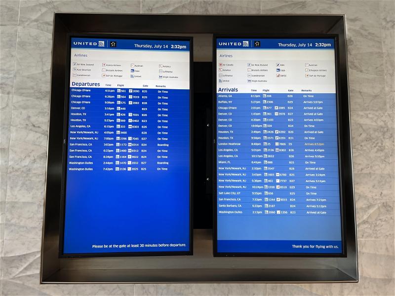 Two monitors showing flight information on a wall.