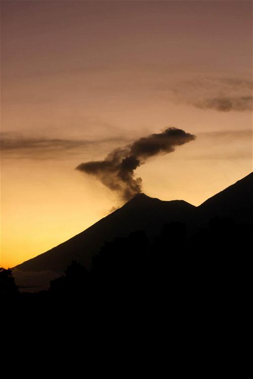 A silhouette of a mountain with smoke coming out of it.