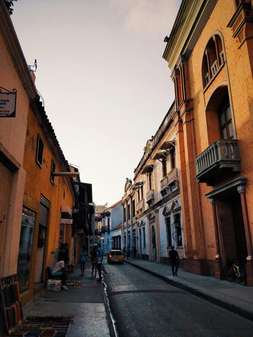 A street with buildings and people walking down it.