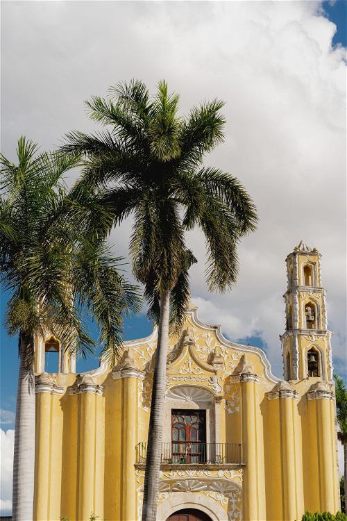 A yellow church with palm trees in front of it.