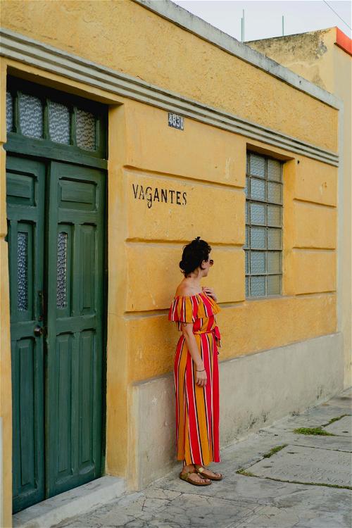 A woman in a striped dress standing next to a yellow building.