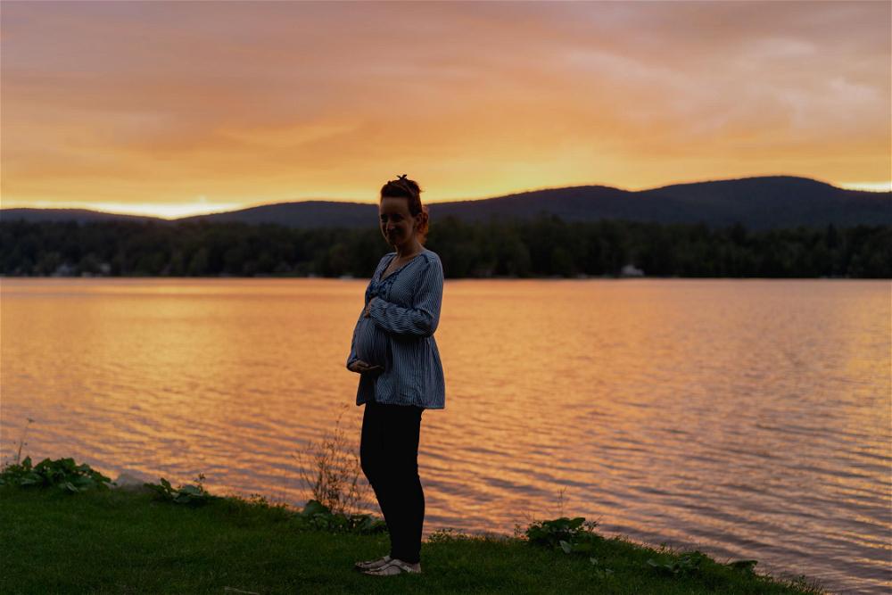 A woman standing in front of a lake at sunset.