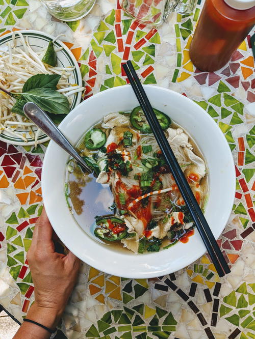 A person holding a bowl of soup with chopsticks.