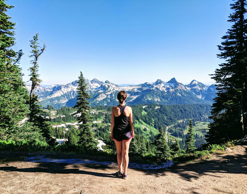 A woman is standing on top of a mountain looking at the mountains.