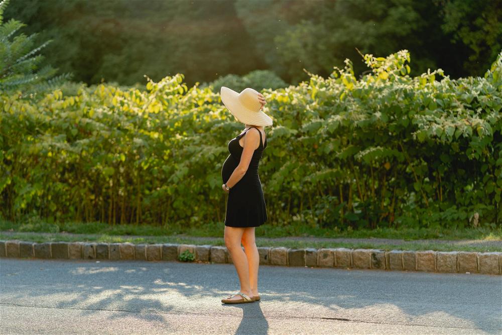 A woman in a black dress and a straw hat is standing on the side of the road.