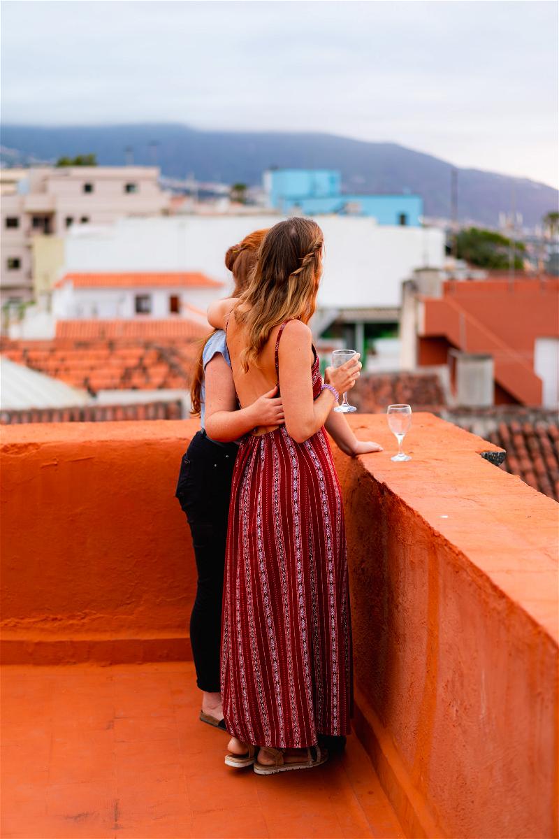 Two women standing on a rooftop overlooking a city.